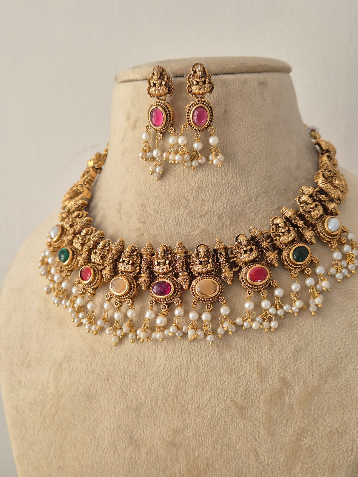 Traditional Indian Ethnic Necklace and Earrings styled against a neutral background, highlighting rich antique gold detailing, vibrant multi-toned stones, and layered pearl accents by Naitri.in