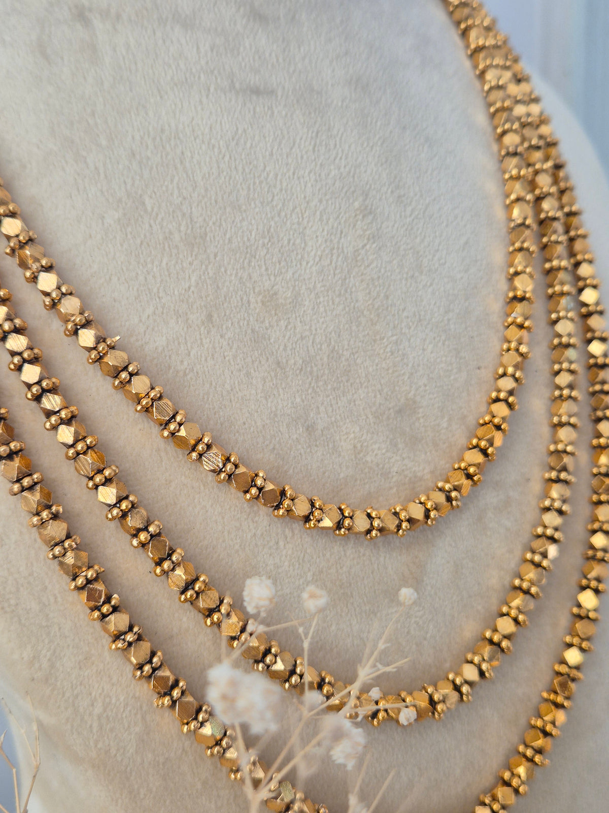 Close-up of a traditional Indian three-layer gold-toned necklace set featuring detailed texturing by Naitri.in