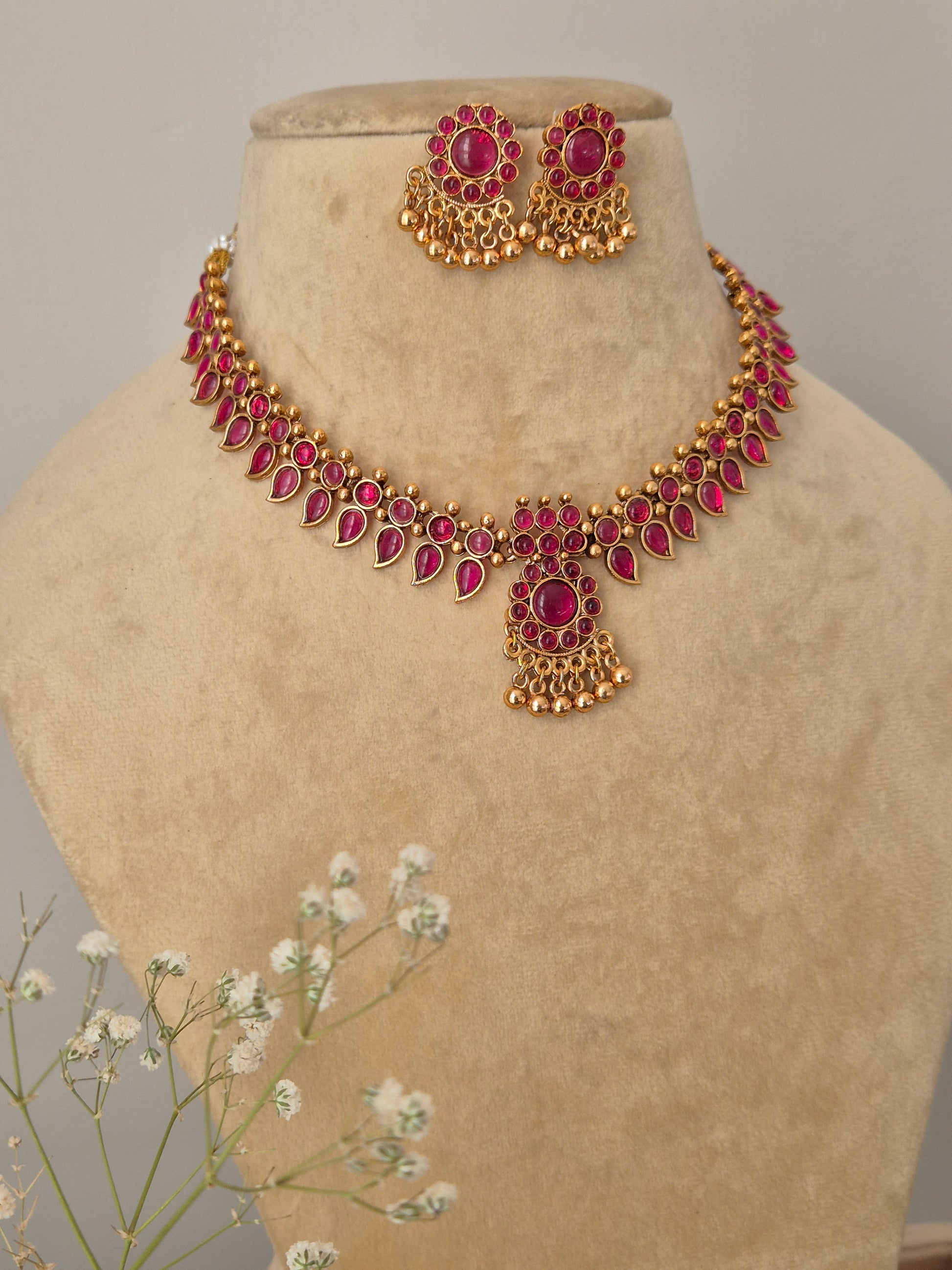 A gold and red stone-studded choker with intricate metalwork and matching teardrop earrings by naitri.in