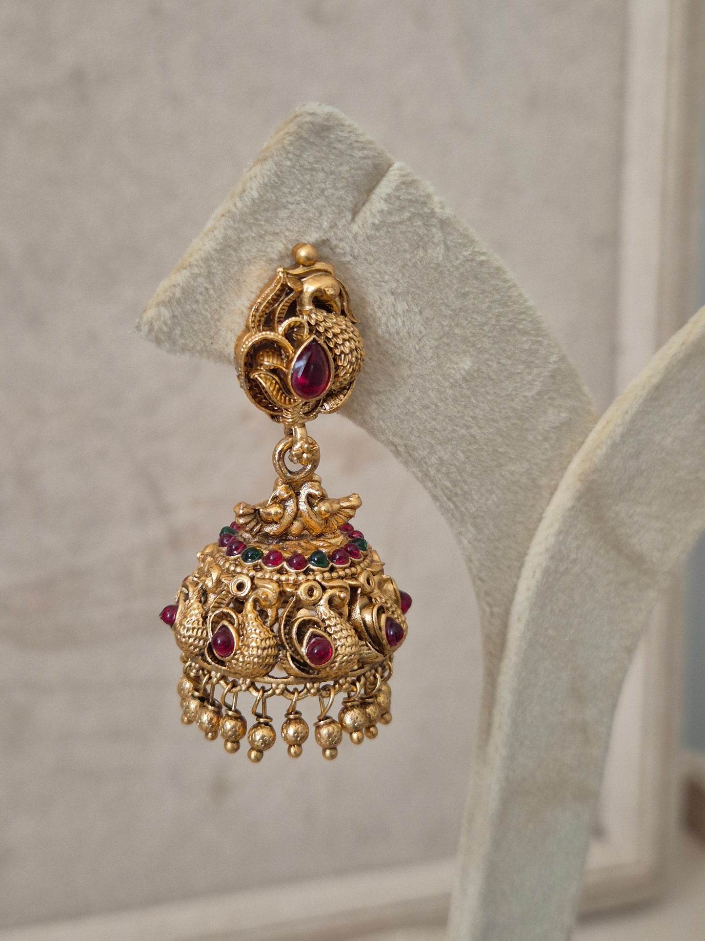 Handcrafted antique gold jhumka earrings with a teardrop pink stone stud, peacock engravings, and delicate metallic gold bead droplets by naitri.in