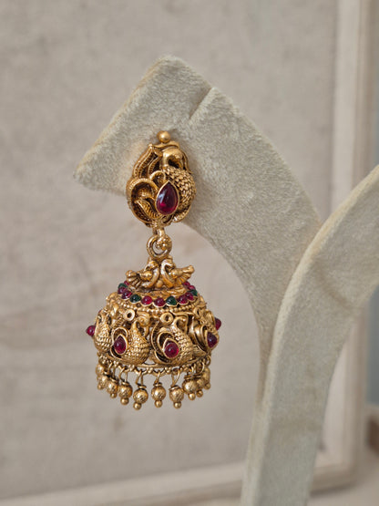 Handcrafted antique gold jhumka earrings with a teardrop pink stone stud, peacock engravings, and delicate metallic gold bead droplets by naitri.in