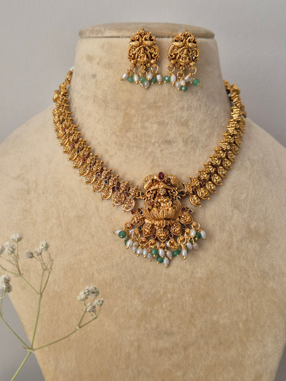 Handcrafted gold temple necklace and earring set featuring green stone accents and hanging pearl fringes by naitri.in