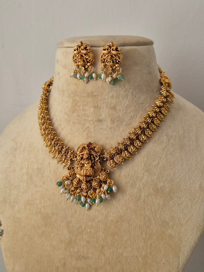 Nandani Temple Jewellery Set: Gold-finish brass necklace with a central deity pendant, colorful stone embellishments, and coordinating stud earrings by naitri.in