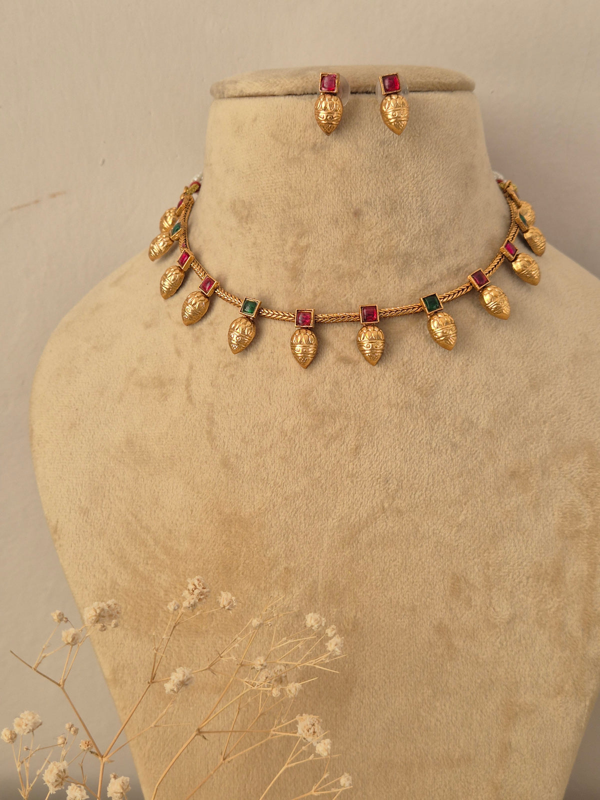 Gold-toned traditional jewelry set with teardrop-shaped gold beads and rectangular red-green stones, by naitri.in