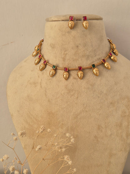 Gold-toned traditional jewelry set with teardrop-shaped gold beads and rectangular red-green stones, by naitri.in
