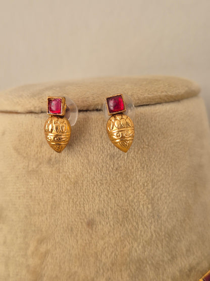 A pair of gold post earrings with a textured, lotus-like gold top and a square pinkish-red gemstone in a beaded border setting, by naitri.in