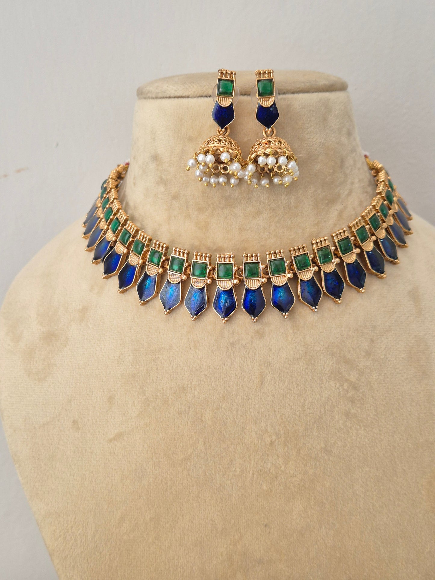 Elegant multi-colored gemstone and gold-toned ethnic choker necklace set, showcased on a minimalist mannequin display next to a sprig of small white flowers by naitri.in