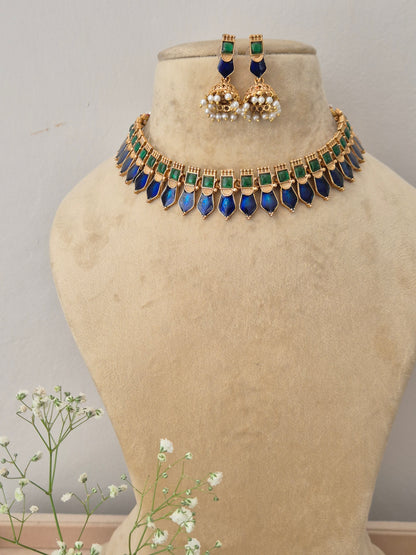 A gold-plated choker necklace featuring a row of square green stones and dangling pointed blue gemstones, with matching jhumka earrings by naitri.in