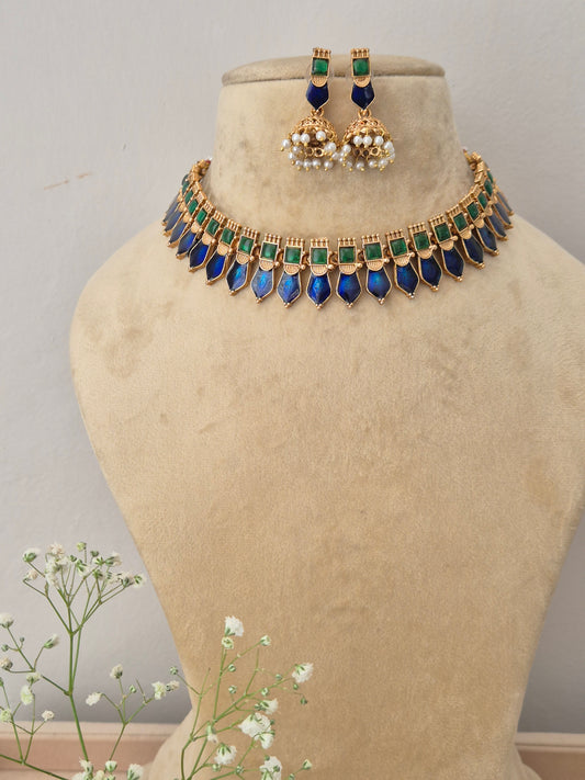 A gold-plated choker necklace featuring a row of square green stones and dangling pointed blue gemstones, with matching jhumka earrings by naitri.in