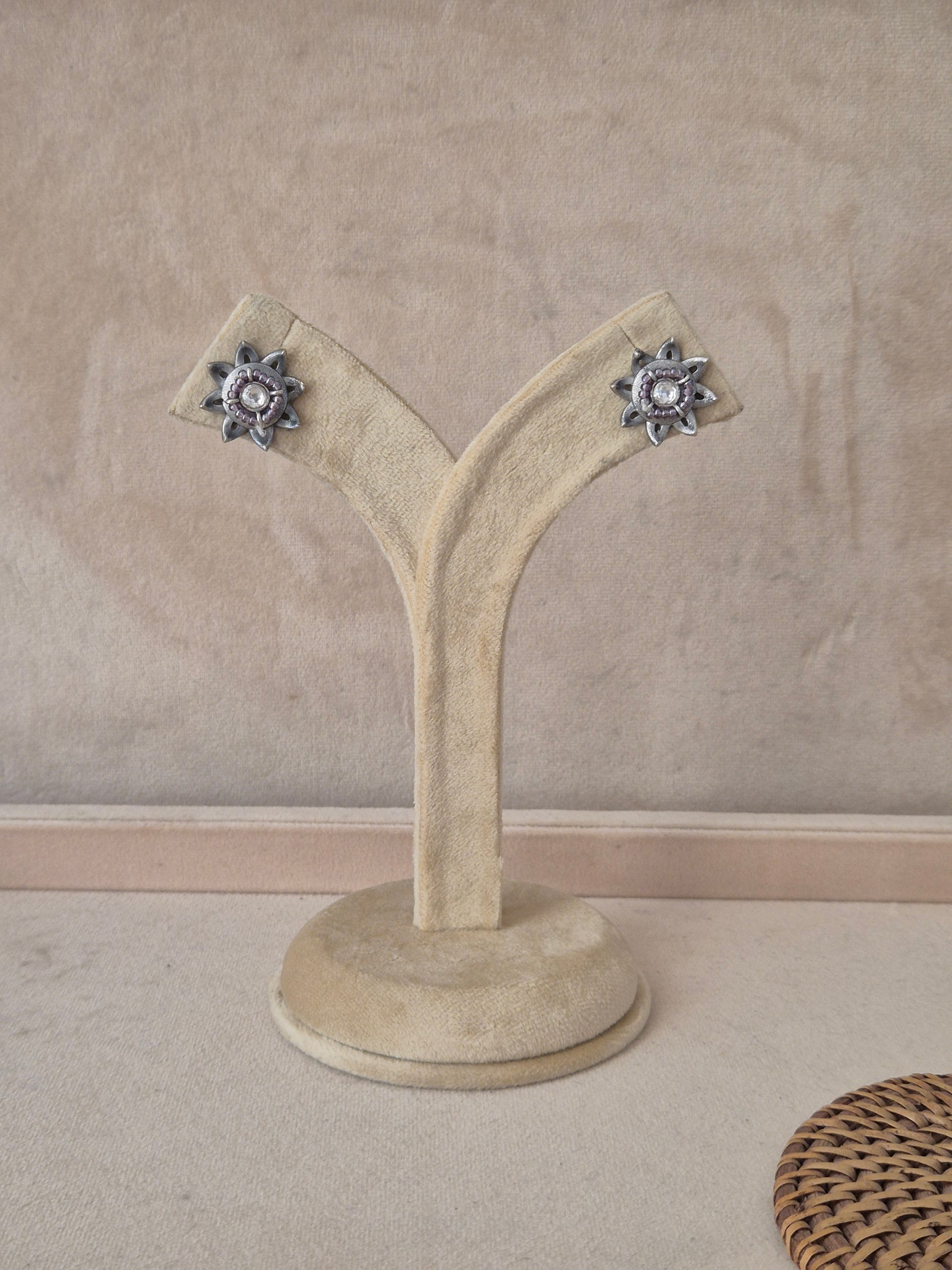 Pair of Neerja silver-toned floral stud earrings featuring an intricate starburst design with a central white stone by naitri.in