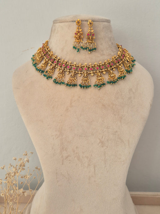 Traditional gold temple choker necklace set with pink/ruby stone accents and green bead drop fringe, with matching dangle earrings by naitri.in