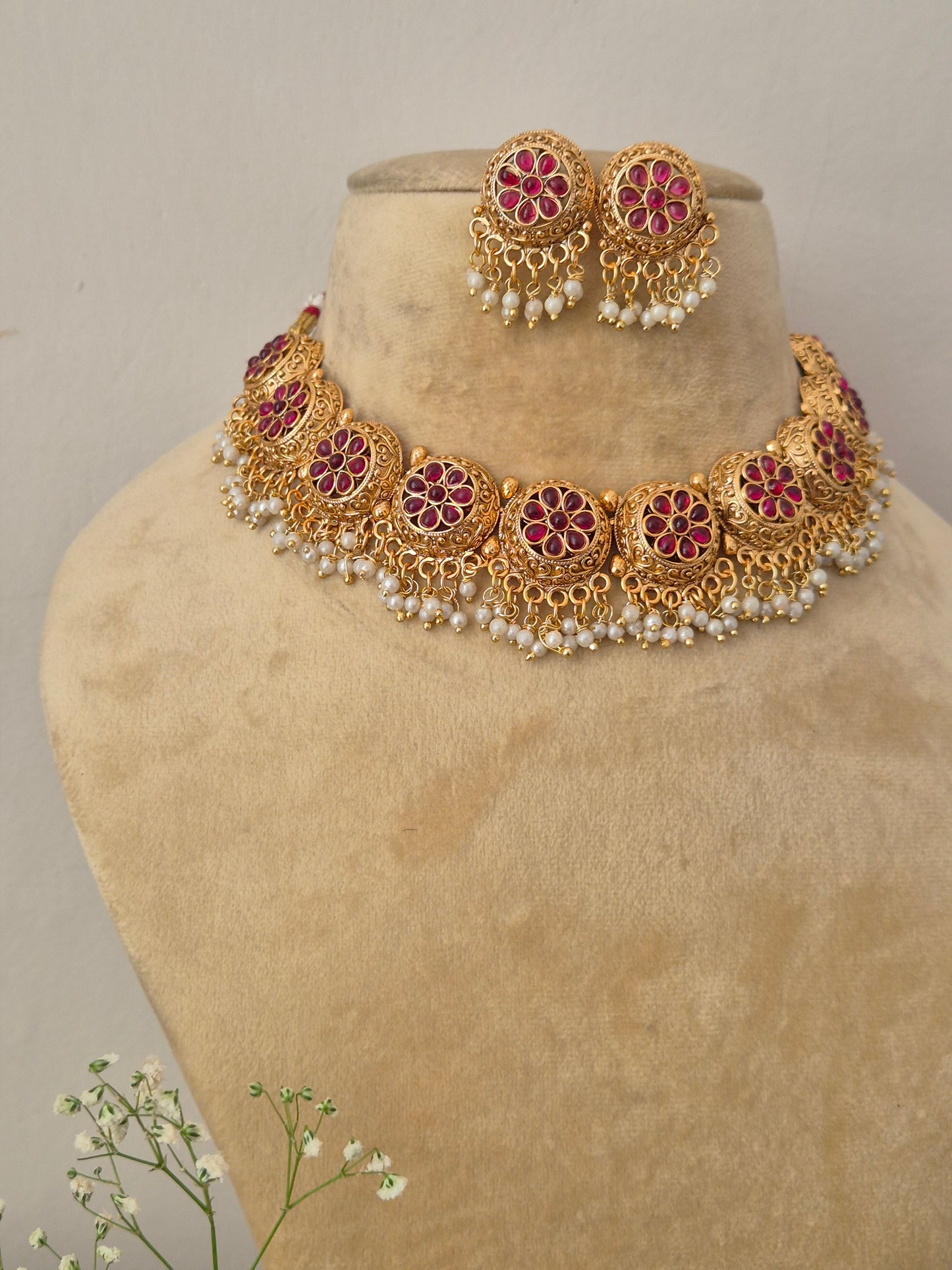 Floral gold necklace adorned with side design like bunches and red studded flower charms by naitri.in