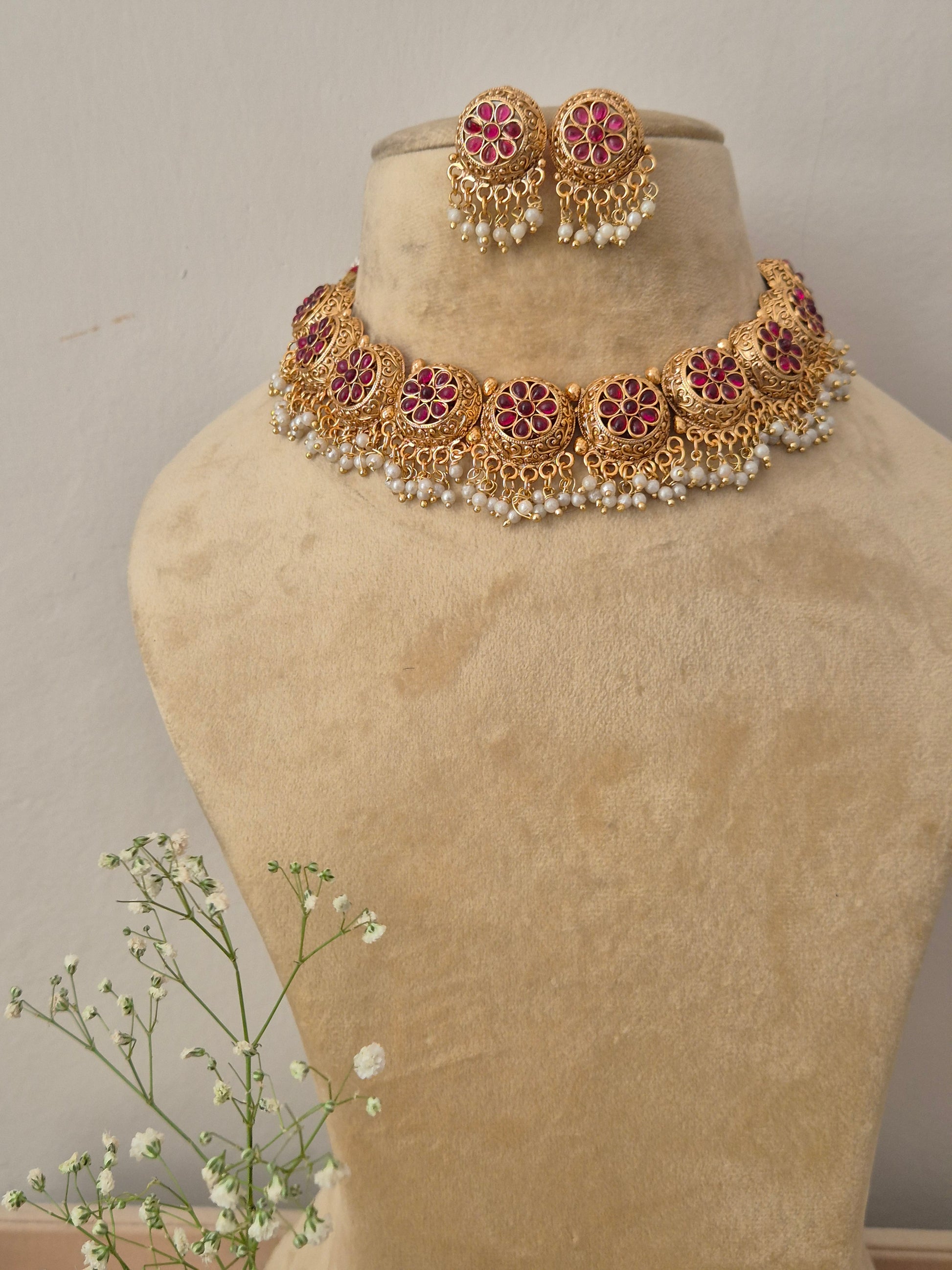 Gold necklace with red gemstones stone in the middle of the flower many golden beads hanging down by naitri.in