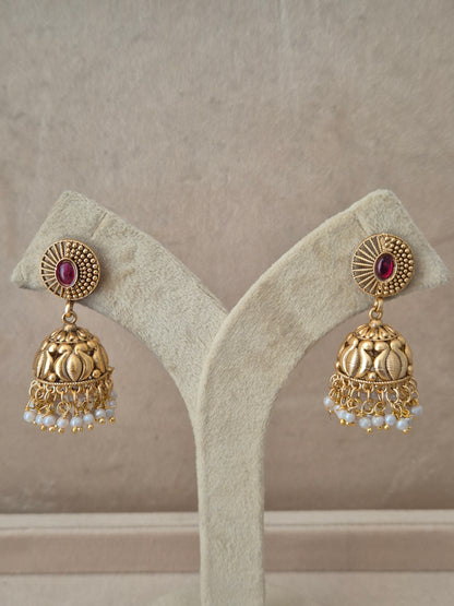 Close-up of Naitri Nivedita premium gold ethnic earrings showcasing traditional Indian Jhumka craftsmanship with a ruby pink stone accent and delicate pearl bead fringe. by naitri.in