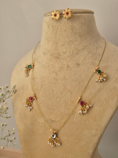 Minimalist gold necklace with five hanging stone pendants in emerald green and ruby red, paired with small round floral-patterned stud earrings.