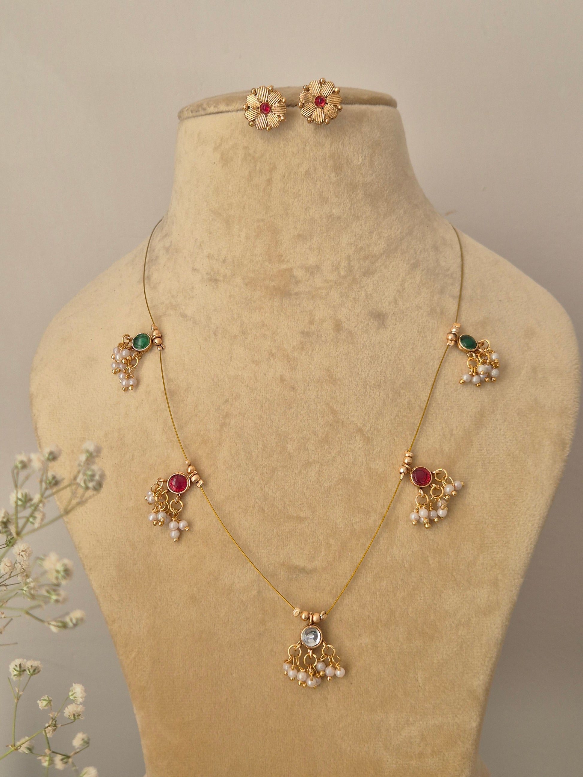 Noor invisible chain necklace set with red, green, and white stone charms and matching floral stud earrings on a gold-tone brass alloy by naitri.in