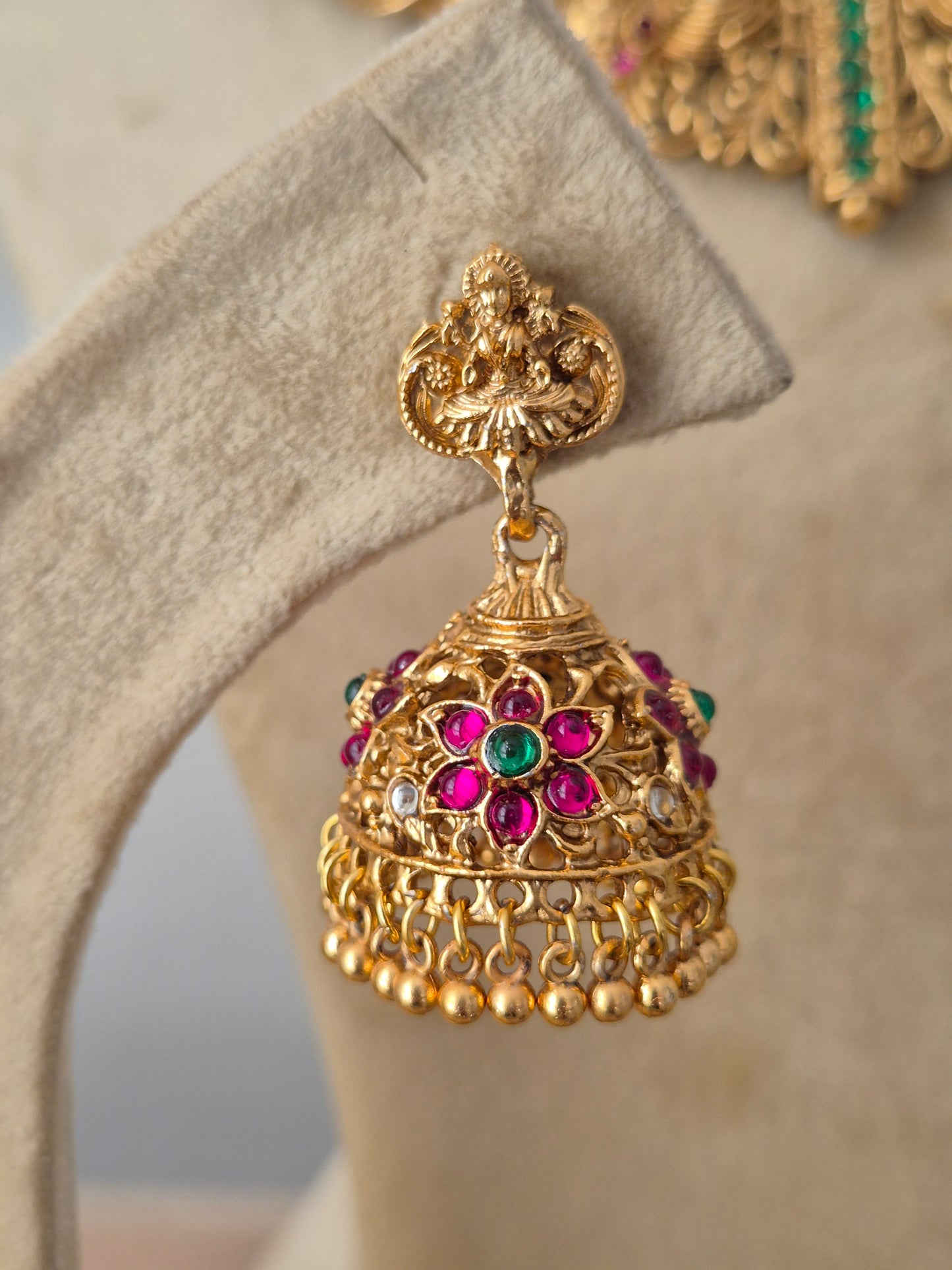 An ornate gold-toned traditional Indian jhumka earring decorated with pink and green gemstone accents for festive wear by naitri.in