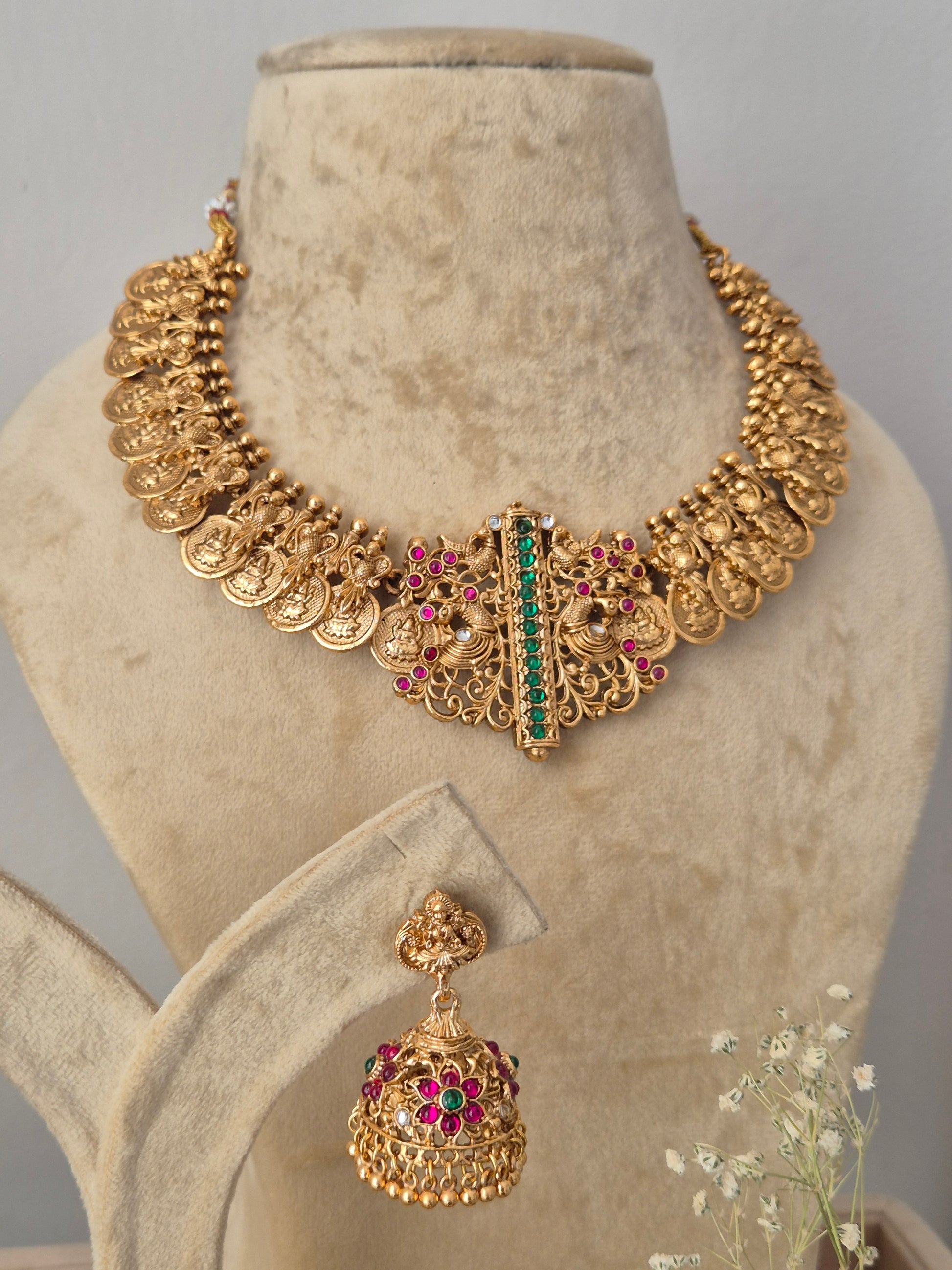 Gold-toned traditional Indian jewelry set featuring a wide collar necklace and matching jhumka earrings, decorated with gold coins, filigree, and red and green stones, by naitri.in