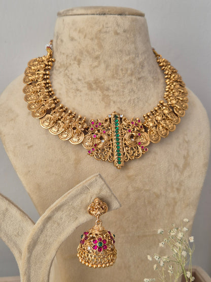 Gold-toned traditional Indian jewelry set featuring a wide collar necklace and matching jhumka earrings, decorated with gold coins, filigree, and red and green stones, by naitri.in
