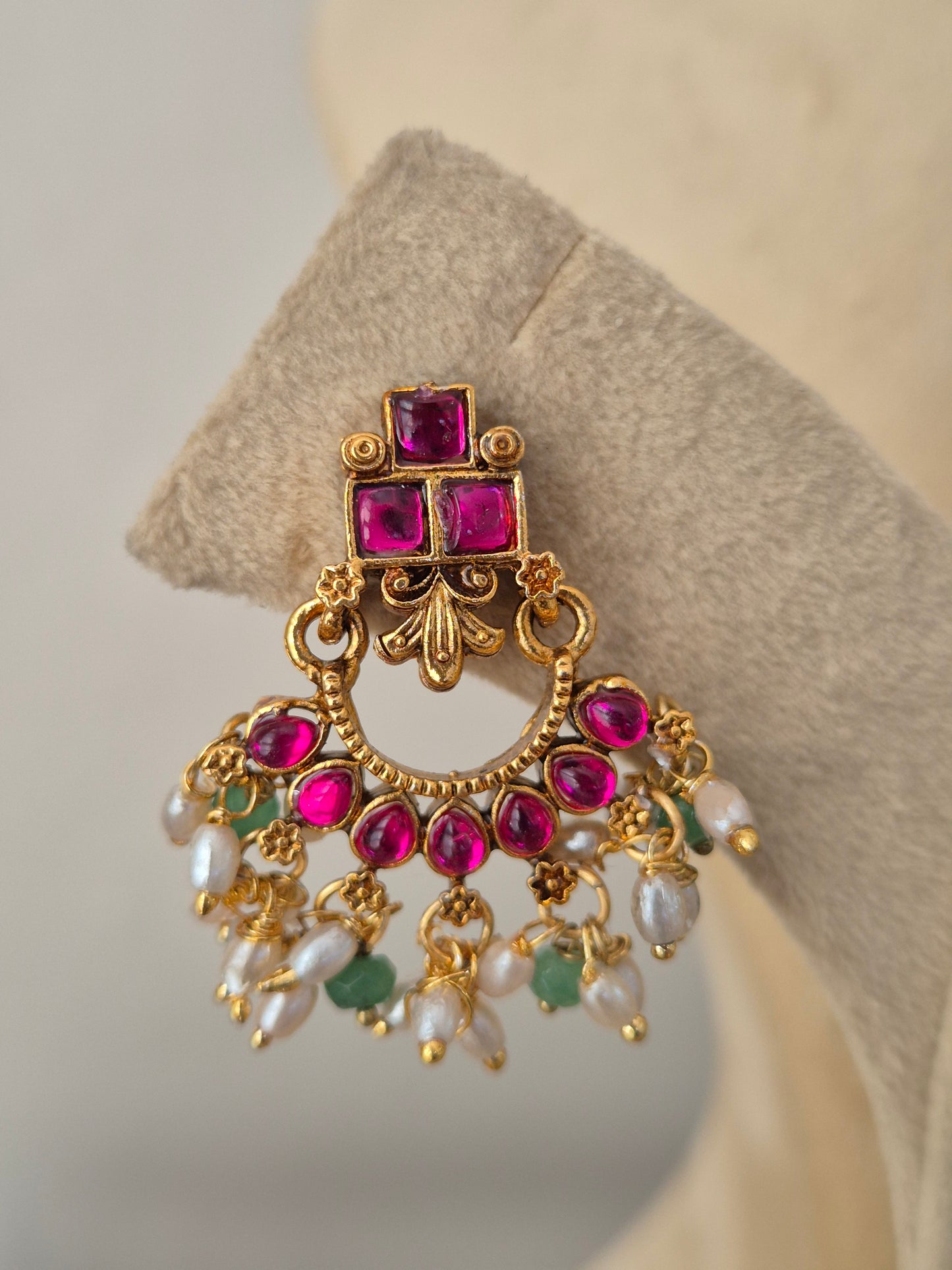 An ornate gold-toned earring with multiple pink gemstones, white pearl-like drops, and small green stones by naitri.in