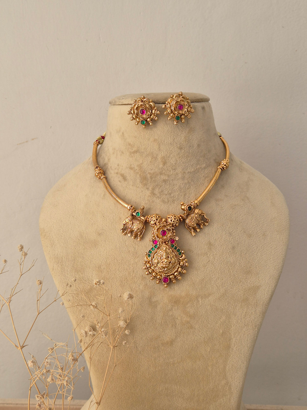 Omika golden ethnic choker necklace set featuring traditional elephant motifs, ruby and emerald gemstone accents, and matching stud earrings by Naitri.in