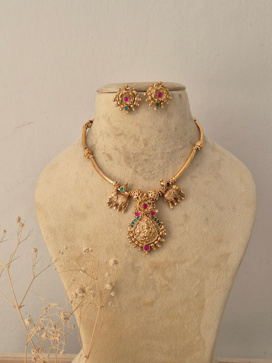 Omika golden ethnic choker necklace set featuring traditional elephant motifs, ruby and emerald gemstone accents, and matching stud earrings by Naitri.in