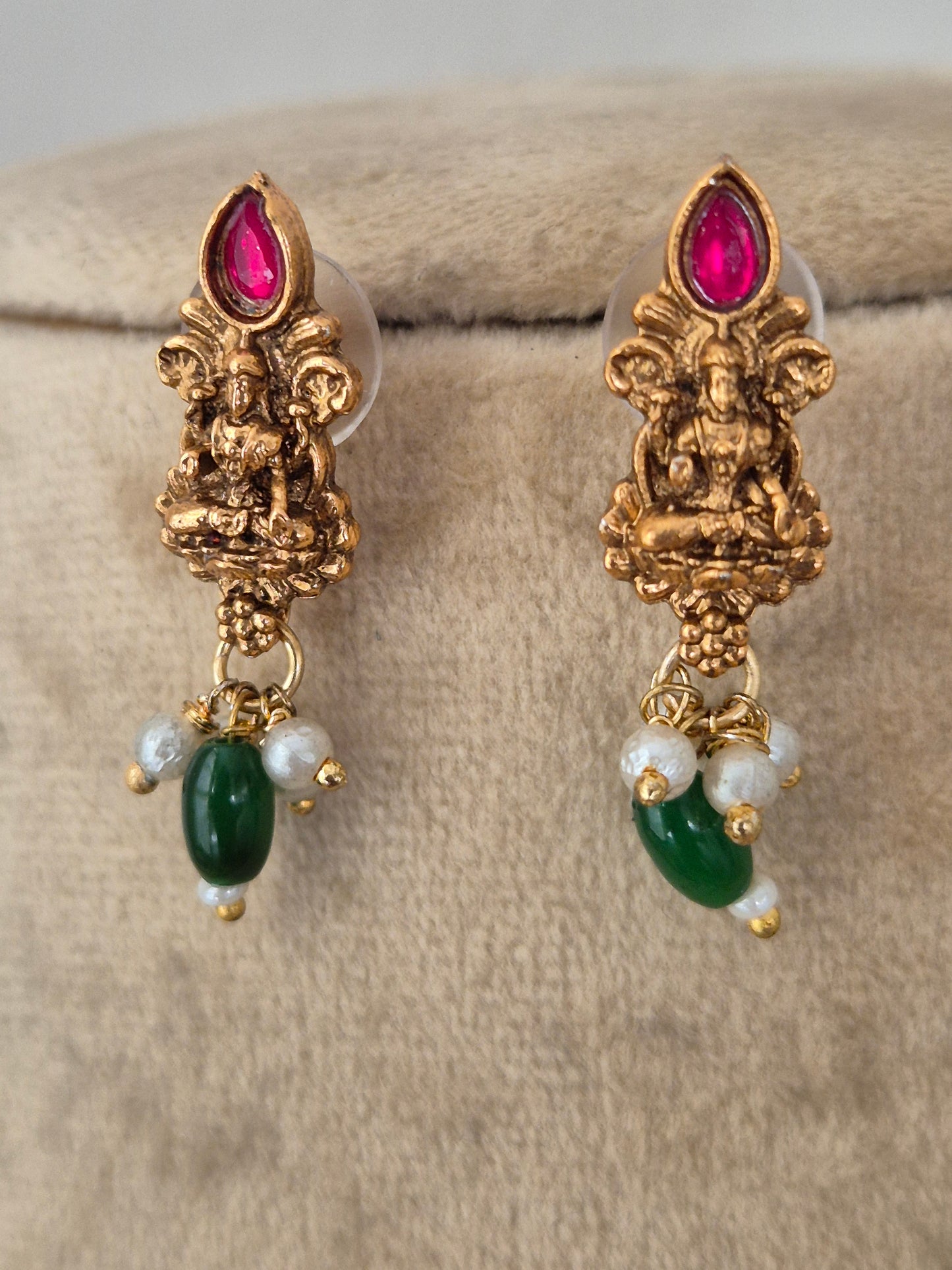 A pair of gold-toned Indian jhumka earrings with Laxmi motifs, featuring pink teardrop gemstones, white pearl-like beads, and green oval stones, by naitri.in