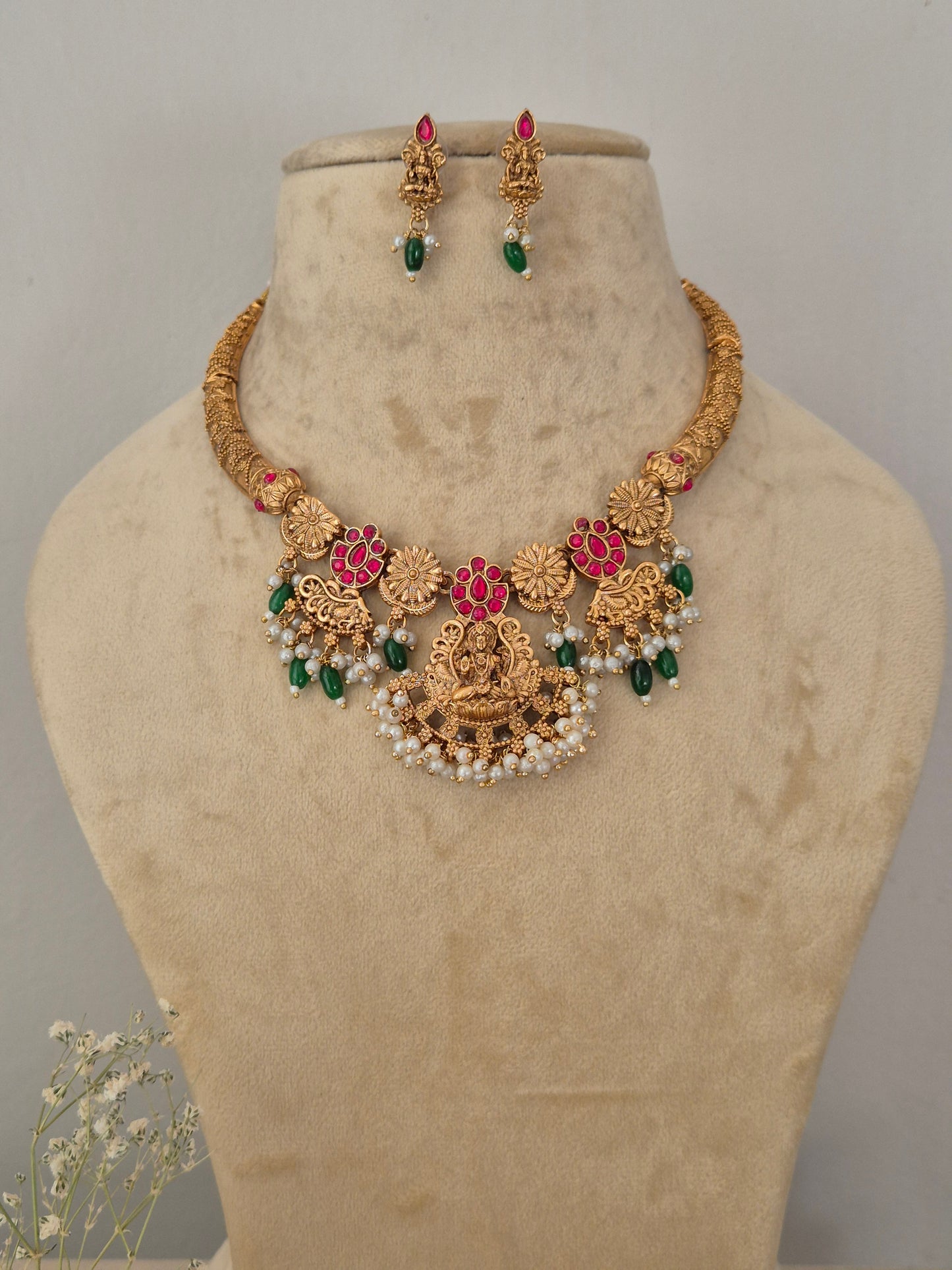 Traditional Indian gold-toned choker necklace set with detailed temple motifs, red and green stone embellishments, and hanging white pearl beads by naitri.in
