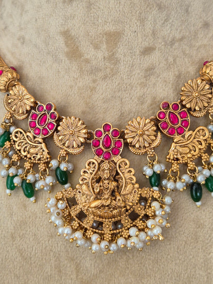 An ornate gold-toned traditional necklace with red gemstone floral motifs, white pearl bead strands, and green bead accents, necklace is designed with intricate floral metalwork, red enamel accents, green gemstones, and a fringe of hanging white pearl-like beads by naitri.in