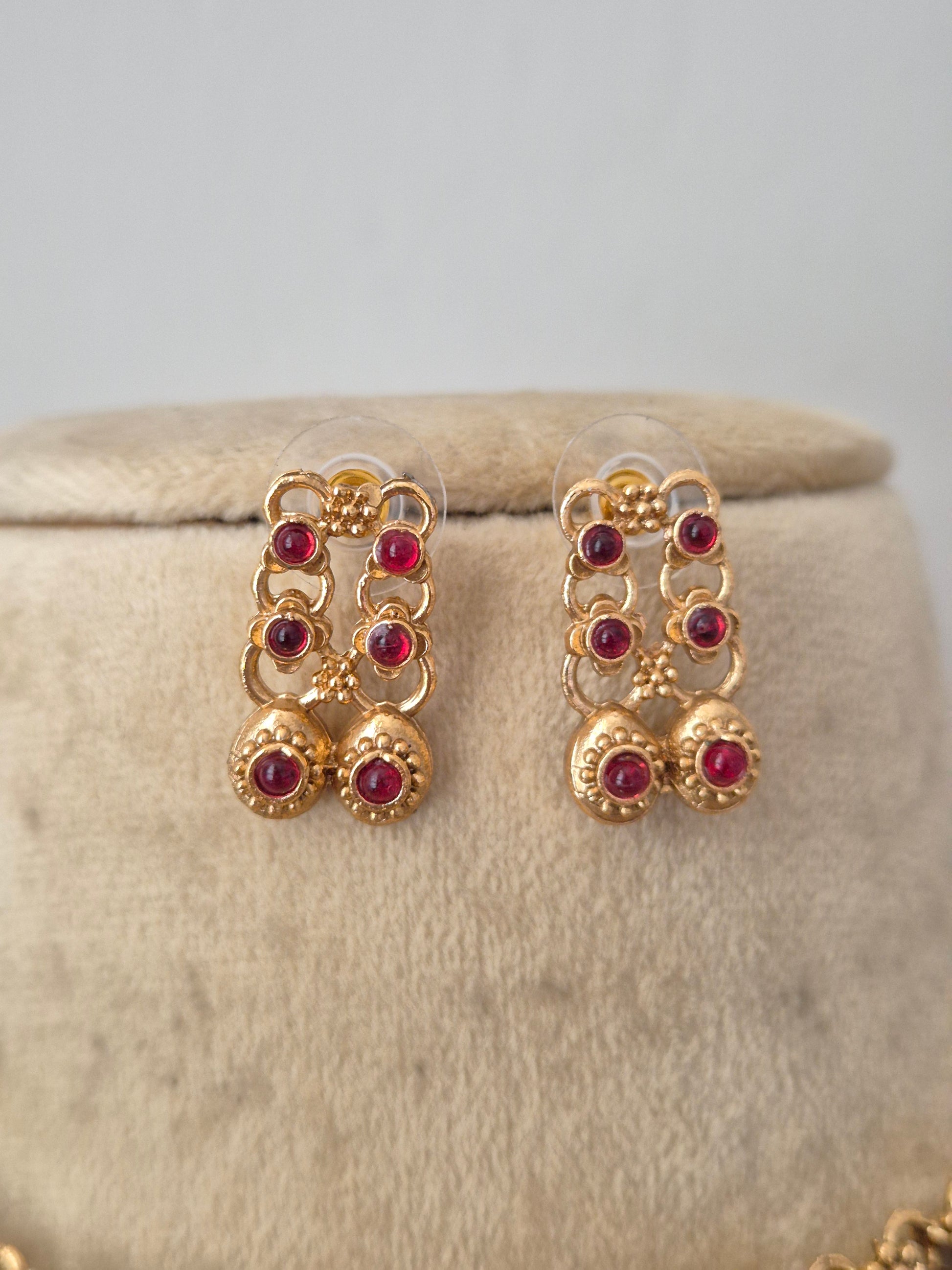 A pair of gold-toned traditional Indian earrings with small red gemstones, by naitri.in