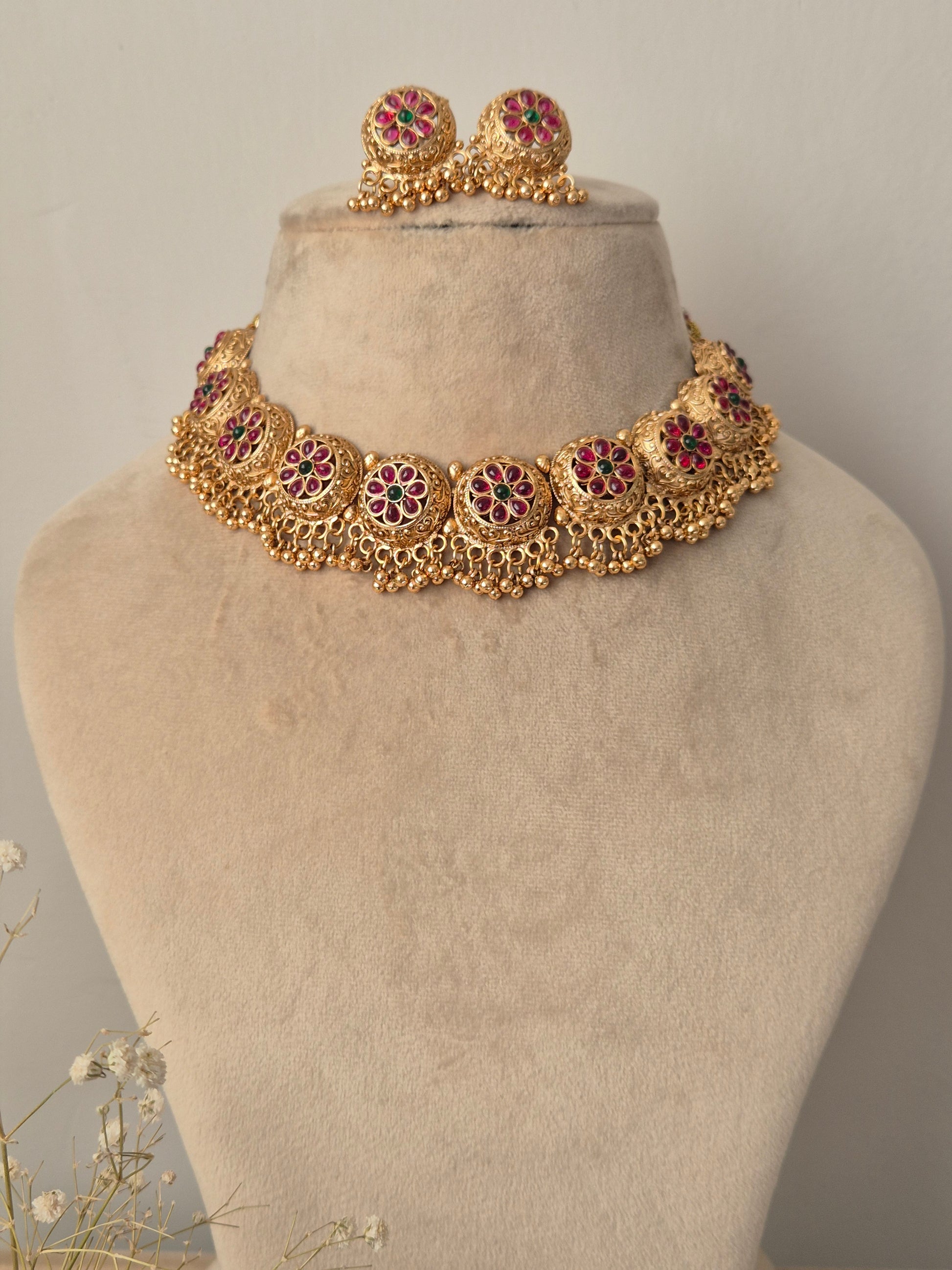 Gold necklace with red gemstones  and green stone in the middle of the flower many golden beads hanging down by naitri.in