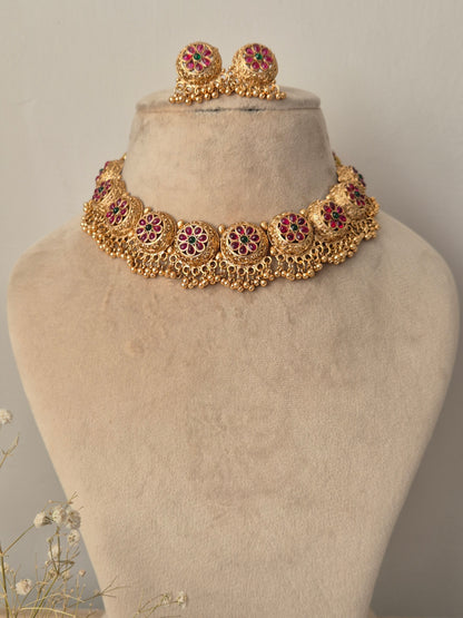 Gold necklace with red gemstones  and green stone in the middle of the flower many golden beads hanging down by naitri.in
