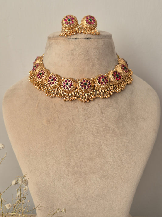 Gold necklace with red gemstones  and green stone in the middle of the flower many golden beads hanging down by naitri.in
