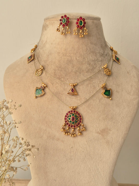 Palki Invisible Chain Necklace Set featuring a golden brass pendant with red and green stones, matching floral stud earrings, and delicate gold charms on a clear invisible chain by naitri.in