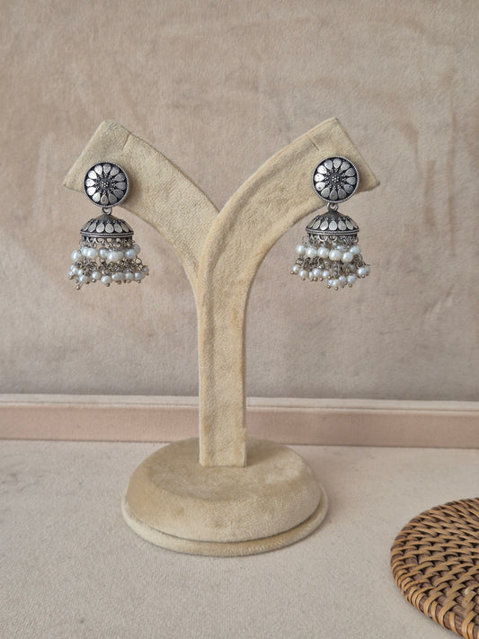 Pair of silver-toned jhumka earrings featuring a wheel-patterned floral stud and white pearl dangles by naitri.in