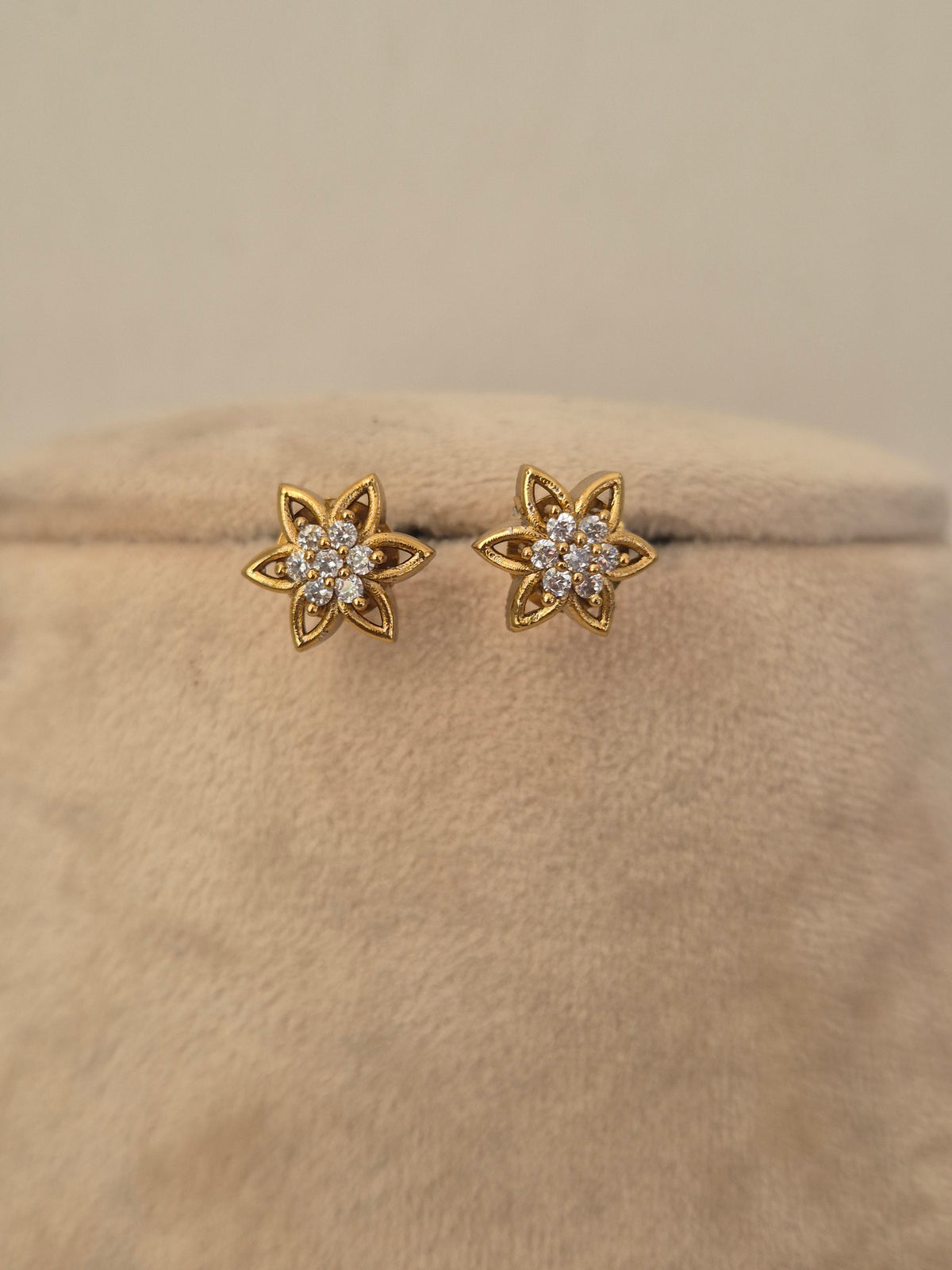 A pair of gold flower-shaped stud earrings with small clear stones in the center, by naitri.in 