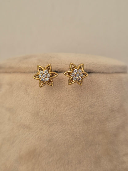 A pair of gold flower-shaped stud earrings with small clear stones in the center, by naitri.in 