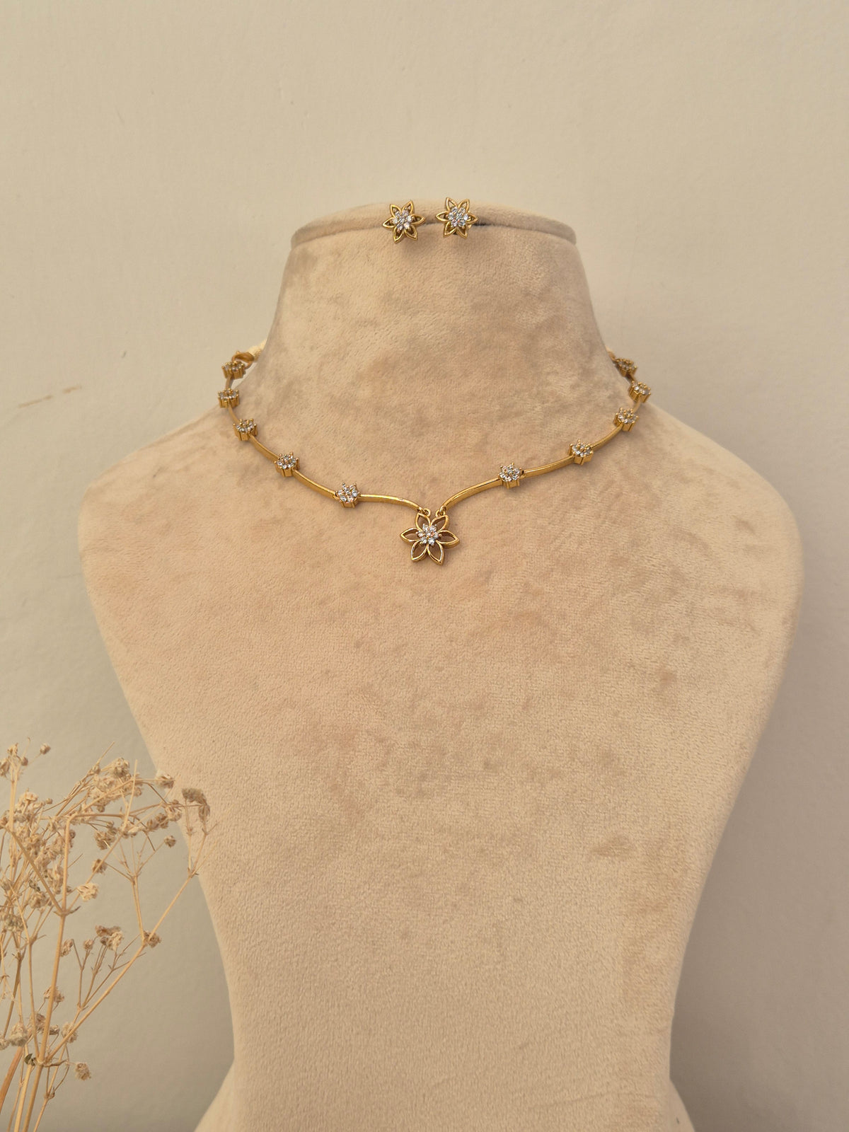 Delicate gold chain necklace with small stone-studded floral stations, a central floral pendant, and matching stud earrings by naitri.in