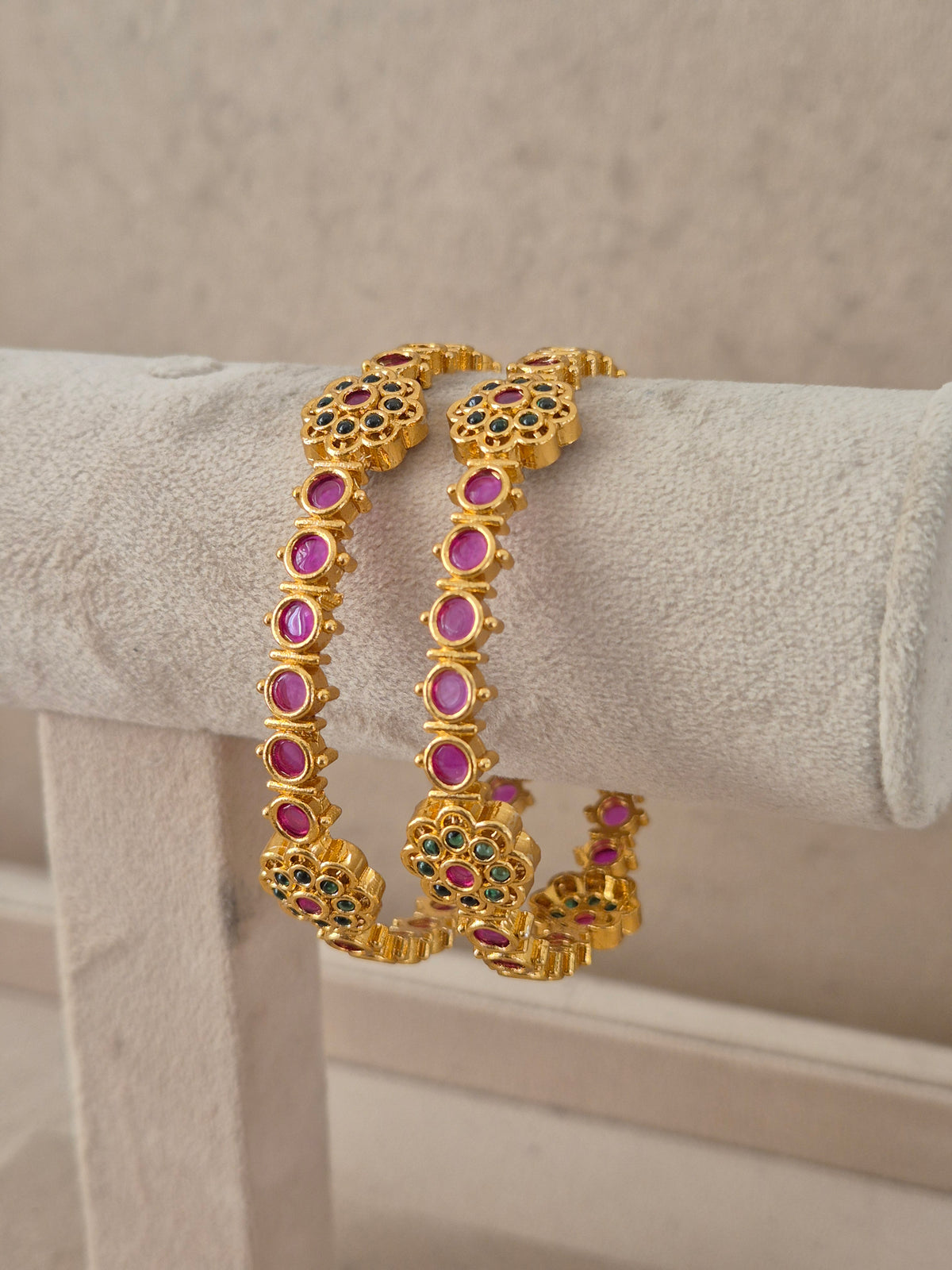 Festive Indian gold-plated bangles featuring intricate floral motifs with red and green gemstone embellishments for weddings and special occasions by naitri.in