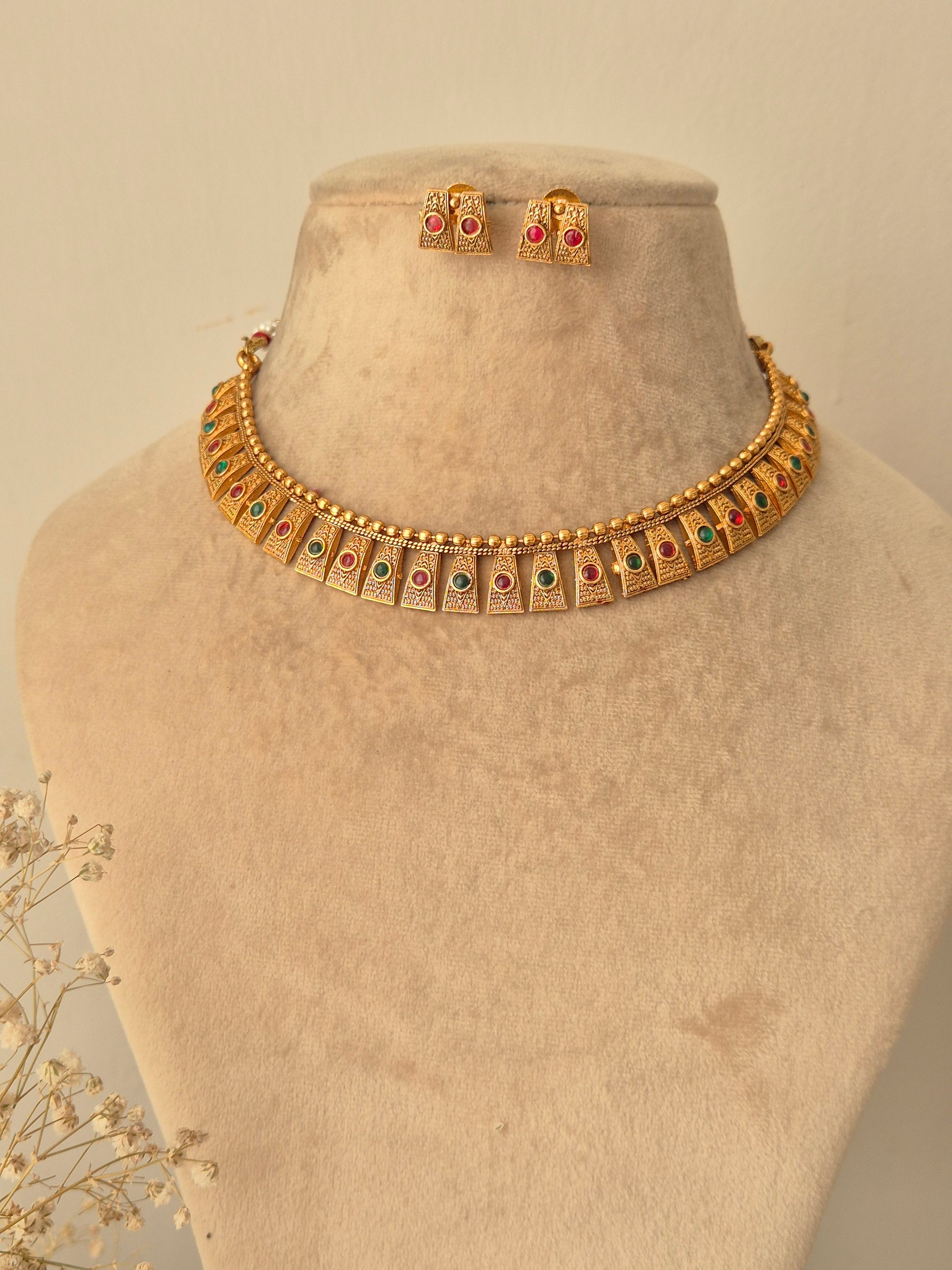 Hammered gold finish necklace set, Close-up of the filigree metalwork and red-green stone settings on a gold-plated brass choker by naitri.in