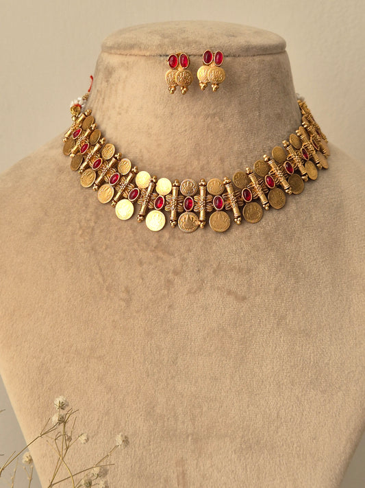 A handcrafted gold-plated choker featuring ruby-red stones and circular gold coin drops with matching ethnic earrings by naitri.in