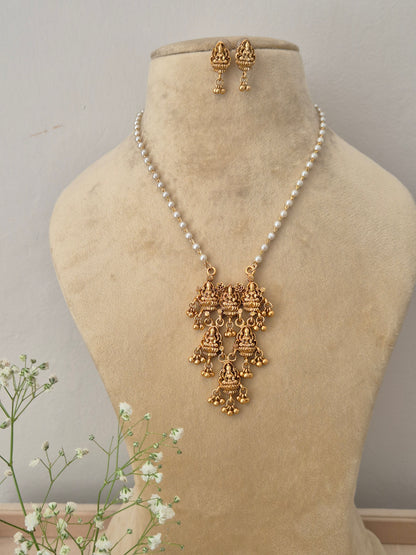 A gold-plated multi-tiered temple jewelry pendant featuring intricate traditional goddess engravings, suspended on a single strand pearl chain with matching earrings by naitri.in