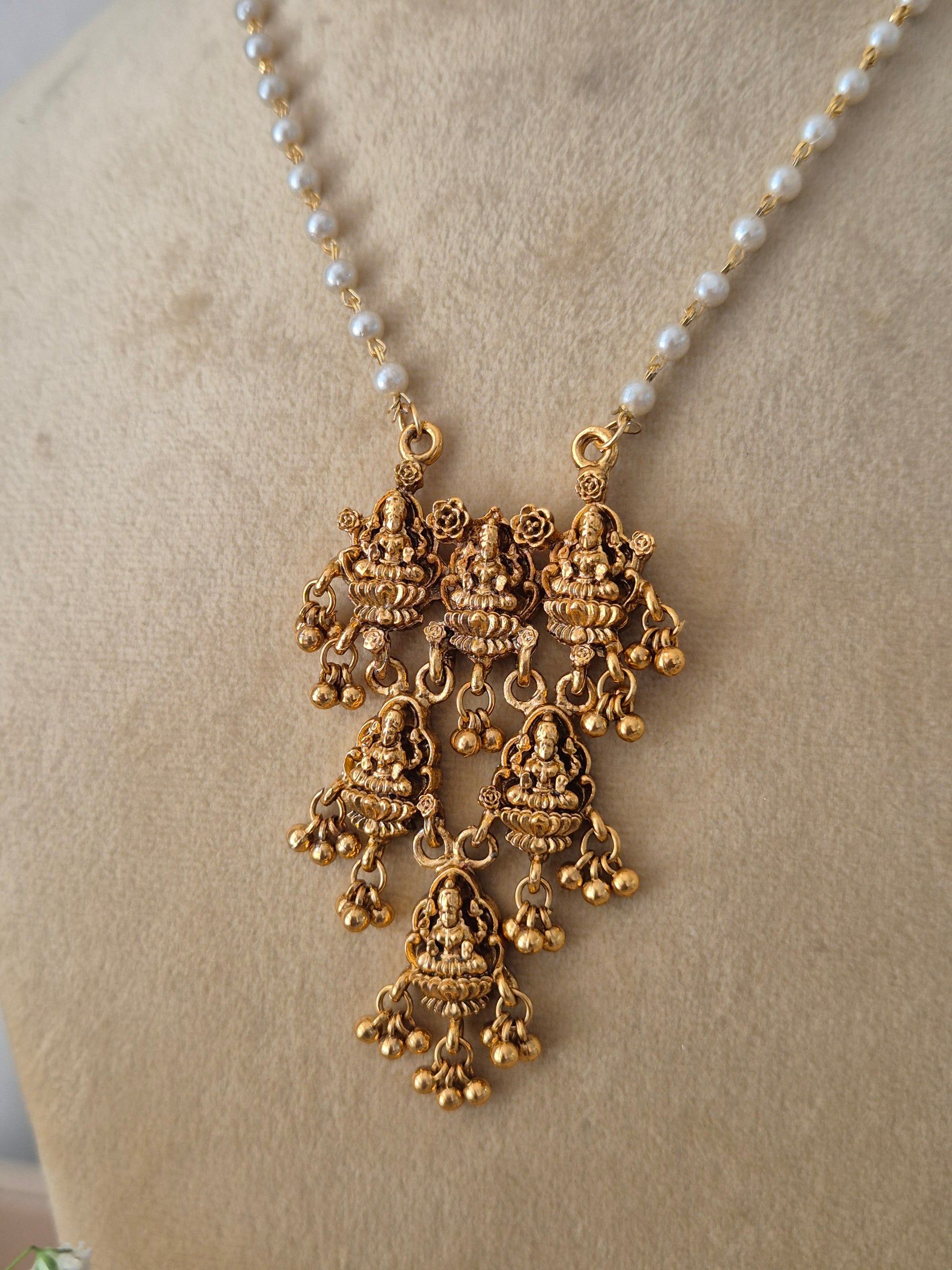 Modern Indian ethnic imitation jewelry set including a golden brass alloy statement pendant with three cascading tiers, attached to a delicate white pearl strand necklace, shown with matching dangling earrings by naitri.in
