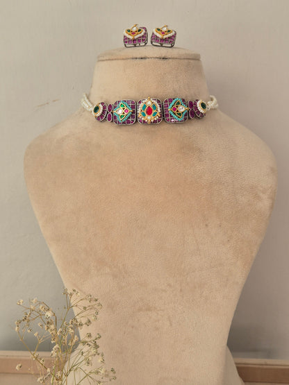 A jewelry set featuring a beaded choker necklace with matching stud earrings. The jewelry has a white base with purple, green, and red beaded geometric patterns. by naitri.in