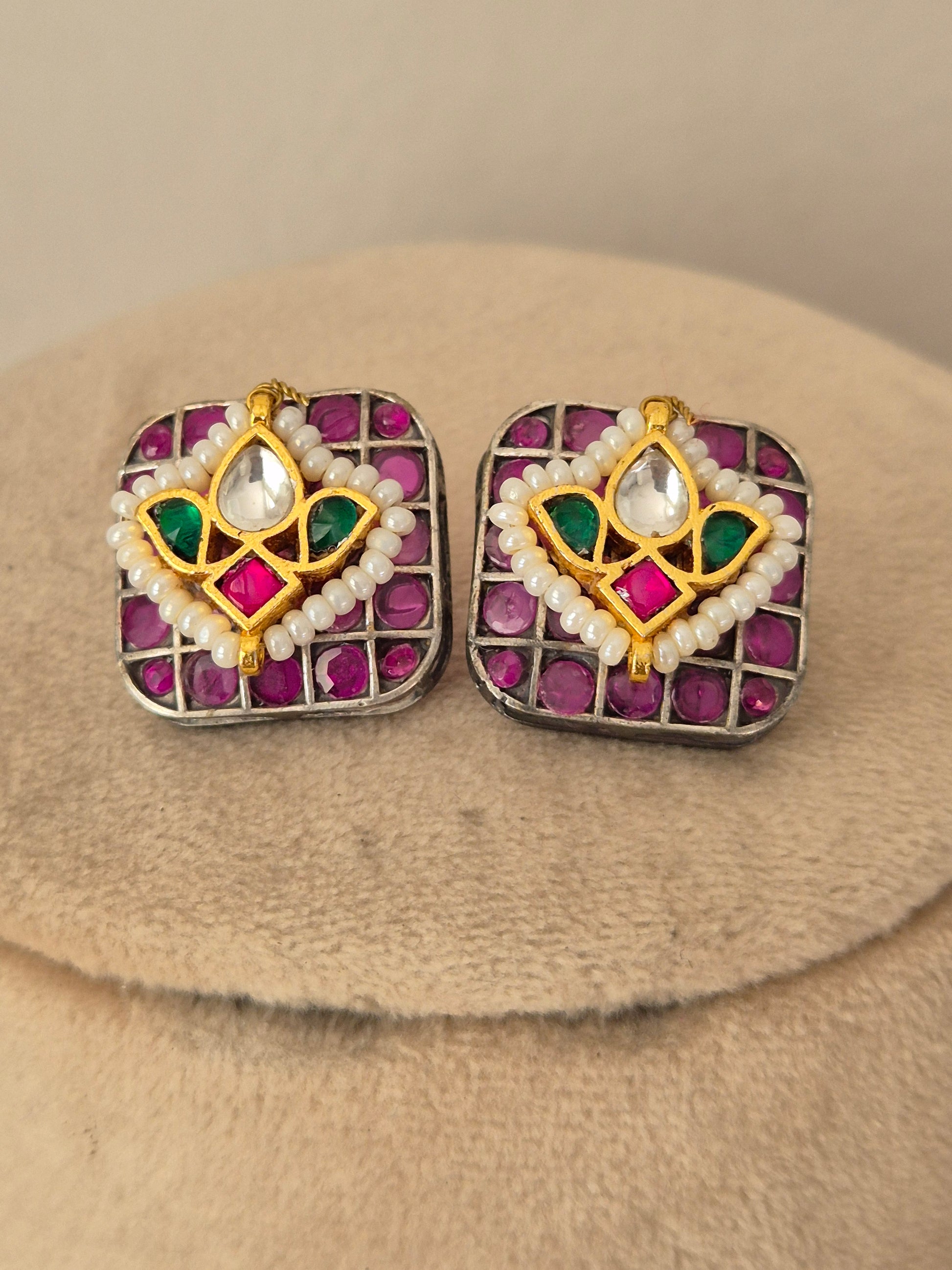 A pair of square gold-toned earrings with pink gemstones, white pearl-like borders, and green and white central motifs by naitri.in