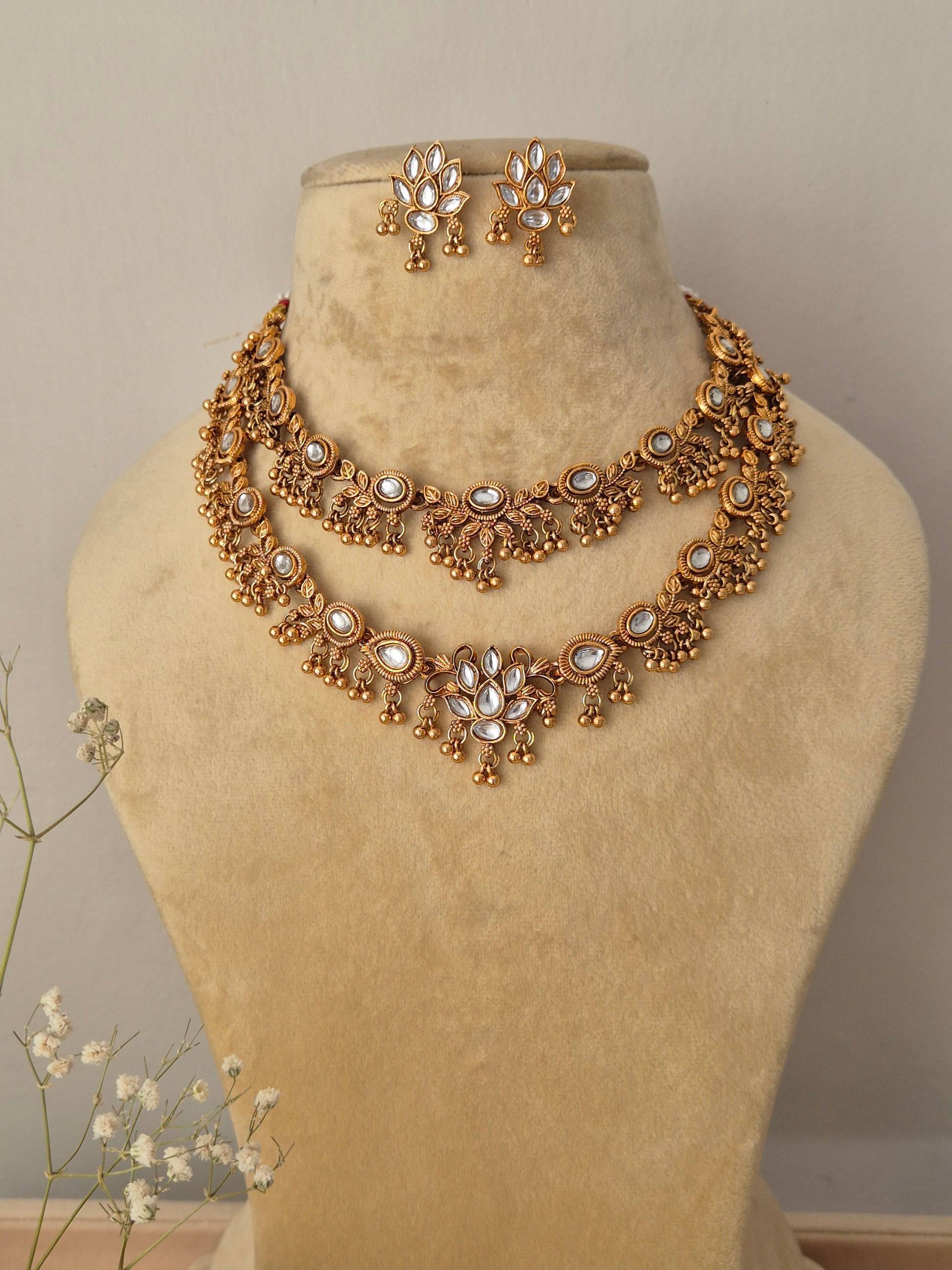 Handcrafted gold-plated double-layered choker necklace featuring kundan-style white stone floral motifs and matching teardrop dangle earrings by naitri.in