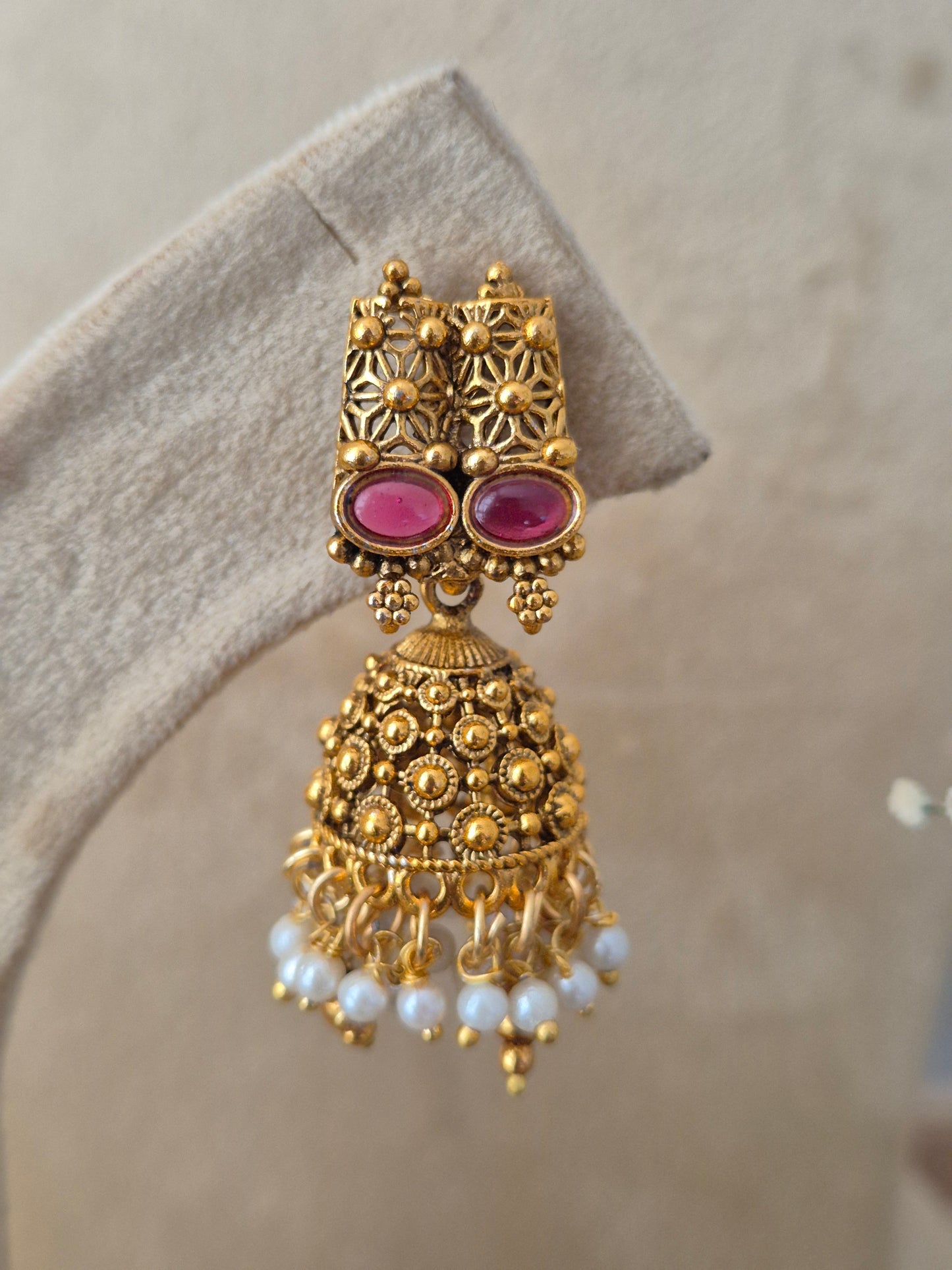 An ornate gold-toned traditional jhumka earring with two oval pink gemstones and dangling white pearl beads, by naitri.in