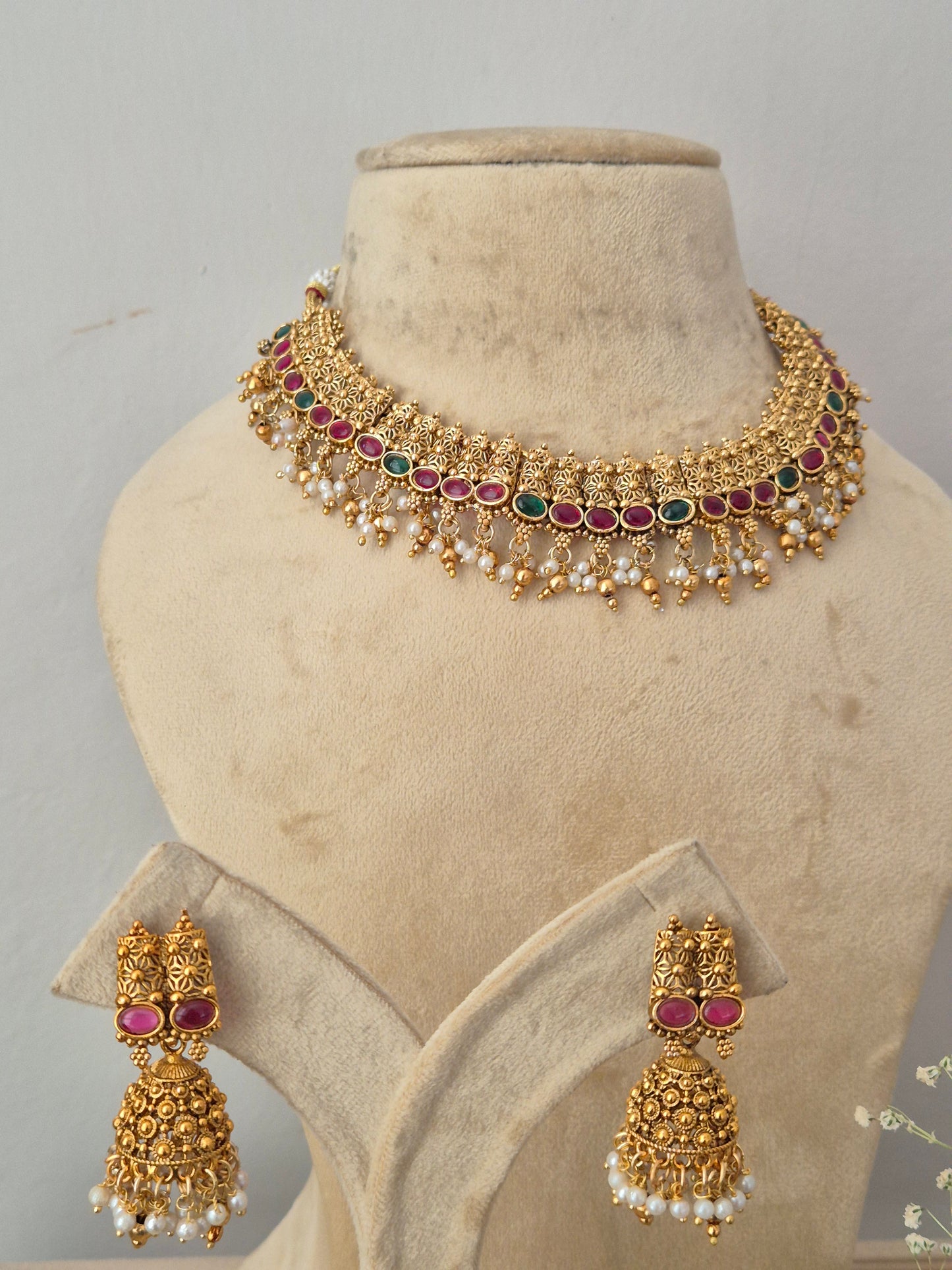 Gold-toned traditional Indian, including a choker necklace and matching earrings with gold filigree, white pearls, and red gemstone accents by naitri.in