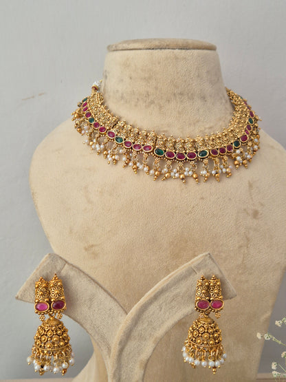 Gold-toned traditional Indian, including a choker necklace and matching earrings with gold filigree, white pearls, and red gemstone accents by naitri.in