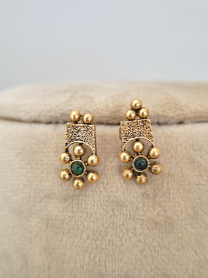 A pair of gold-toned traditional Indian earrings with textured square fronts, small gold beads, and a central round green stone, by naitri.in